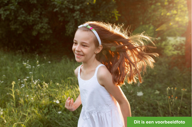 Blij meisje van ongeveer 8 jaar, met wit jurkje aan, rent in het zonnetje door het gras.