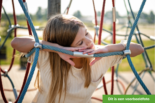 Meisje rond de 8 jaar staat in een speelrek en kijkt dromerig weg.