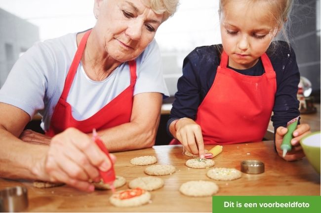 Een oma-figuur en blond meisje bakken samen koekjes