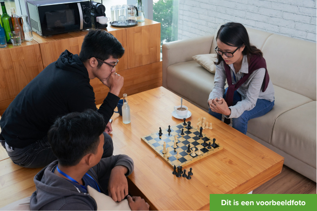 Drie jongvolwassen vrienden spelen schaak aan tafel.