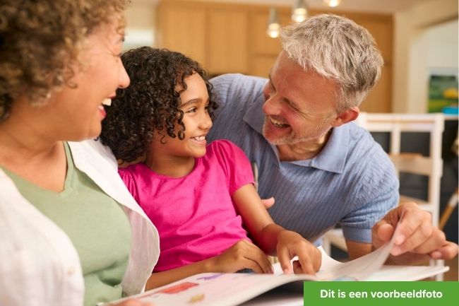 Opa en oma zitten aan tafel lachen en lezen een boek met kleindochter